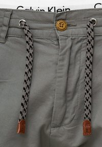 Sive hlače s teksturiranim završetkom, s smešnim dugmetom i uzorkovanim užetom u sivoj i crnoj boji. Calvin Klein logo na pojasu.