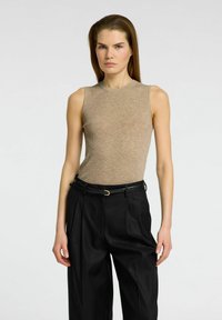 Beige ribbet tanktop med rund halsudskæring, parret med højtaljede sorte plisserede bukser og et slankt sort bælte.