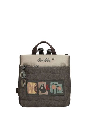 Zaino marrone quadrato con manico superiore, tasca frontale con cerniera, toppa colorata con la scritta "ANEKKE" e portachiavi decorativo.