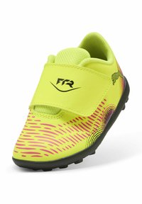 Pantofii de fotbal pentru copii, de culoare galbenă strălucitoare, cu sistem de prindere Velcro, superior texturat din material sintetic cu modele în valuri roz și talpă din cauciuc negru.