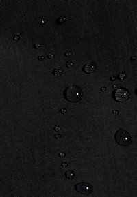 Waterdruppels parelen op gestructureerde zwarte waterdichte stof, die het waterafstotende oppervlak laat zien.