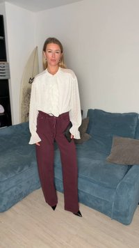 Camisa blanca con frente con volantes y mangas texturizadas, combinada con pantalones burdeos de talle alto. Clutch negro y tacones negros puntiagudos.