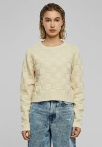 Crème kleurige, textuur-gebreide trui met een schaakbordpatroon, ronde halslijn en geribde manchetten. Gestyled met licht gewassen denim.
