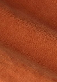 Tissu texturé dans une teinte rougeâtre-orange, avec un motif de tissage subtil et une finition lisse, créant une apparence et une sensation douces.