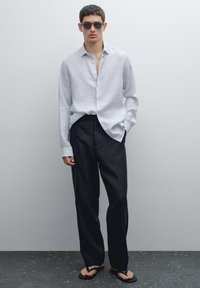 Light gray striped button-up shirt, dark pinstriped wide-leg pants, and black flip-flops. Model wears dark sunglasses. Simple, modern design.
