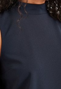 Navy blue sleeveless top with a high neckline, featuring a smooth texture and subtle sheen, designed for a fitted silhouette.