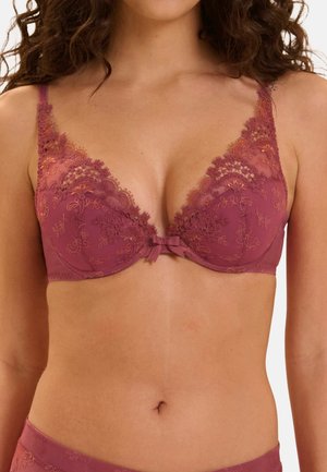Donna che indossa un reggiseno in pizzo malva con ricamo floreale e un piccolo fiocco centrale, mostrando il torso dalle spalle alla vita.