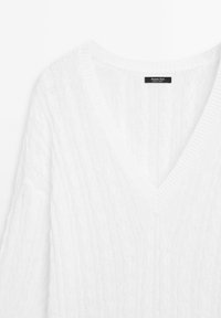 White knitted sweater featuring a V-neck design, cable knit pattern, and ribbed trims. Made from lightweight material.