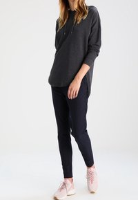 Felpa a maniche lunghe grigio scuro con orlo curvo e lacci, abbinata a leggings a righe navy e scarpe da ginnastica rosa chiaro.