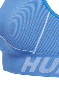 Blå sportbehå med ribbad textur, med en bred elastisk rem med vit logotyp och kontrasterande sömnadsdetaljer. Justerbara axelband.