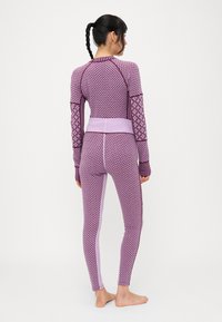 Conjunto deportivo ajustado de color púrpura con mangas largas y leggings a juego. Presenta un diseño texturizado y acentos de colores contrastantes.