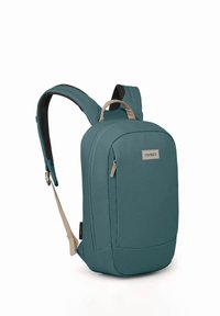 Mochila color teal con un acabado de tela suave, que incluye un zipper lateral, correas acolchadas y un parche de logo. Diseñada para un almacenamiento compacto y comodidad.