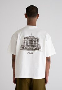 White cotton t-shirt featuring a detailed black illustration of a building on the back, with "Prohibited Grand Resort" text beneath.
