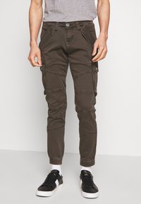 Cargo broek in donker olijf, met taps toelopende pijpen, meerdere zijzakken, gestikte accenten en een knoopsluiting. Duurzame stoftextuur.