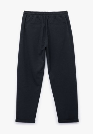 Zwarte jogpants van een gestructureerde stof, met een elastische tailleband en twee achterzakken; de boorden zijn iets opgerold bij de enkels.