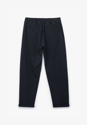 Zwarte jogpants van een gestructureerde stof, met een elastische tailleband en twee achterzakken; de boorden zijn iets opgerold bij de enkels.