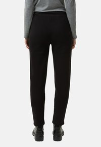 Zwarte tapered broek met een elastische tailleband, gemaakt van een zachte stof. Heeft een gladde textuur en een minimalistisch ontwerp, zonder zichtbare zakken.