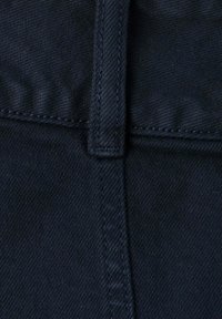 Gros plan sur un tissu en denim foncé montrant une couture verticale et une boucle de ceinture cousue.