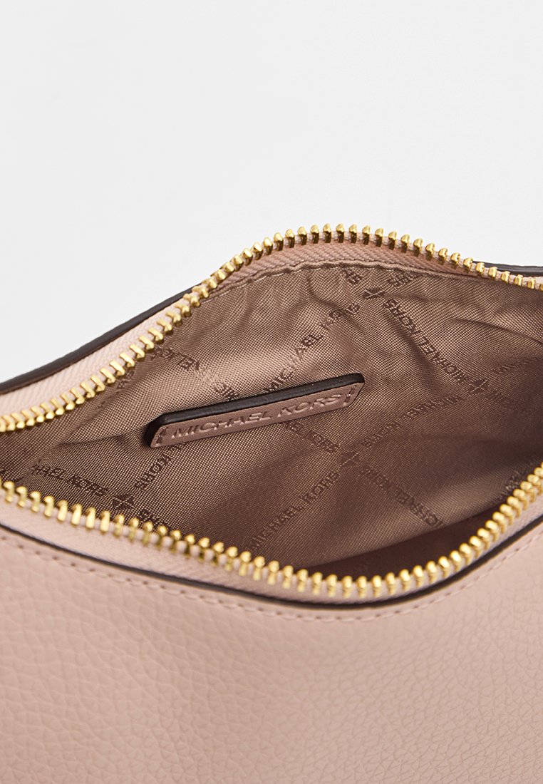 Beige Leder-Tascheninnenseite mit goldenem Reißverschluss, ausgestattet mit einem glatten Futter und einem geprägten Markenlogo auf einem rechteckigen Lederschild.