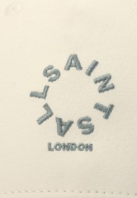 Hvidt stof med cirkulær broderi i lyseblå, der staver "SAINT LONDON" med variende højder på bogstaverne. Glat tekstur, ingen yderligere accenter.