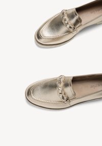 Mocassins en cuir doré métallique avec détail de bride tressée et bout arrondi, présentés sur un fond blanc.