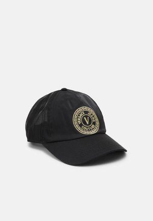 Casquette de baseball noire à visière incurvée, avec un patch rond brodé en or portant l'inscription « Versace Jeans Couture » sur le devant.