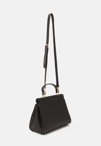 Mustassa nahkakäsilaukussa on jämäkkä muotoilu, yläkahva ja säädettävä hihna. Kultaisen väriset metalliosat tuovat yksityiskohtia laukkuun.