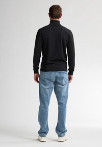 Schwarzer Rollkragenpullover mit langen Ärmeln, kombiniert mit hellblauen geraden Jeans. Weiße Sneaker runden das lässige Outfit ab.