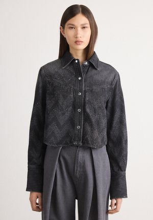 Veste en denim noire cropped avec un motif en chevron, ornée de clous en argent, dotée d'une fermeture à boutons et d'un col pointu.