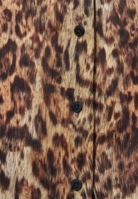 Tissu à imprimé léopard avec une surface douce et texturée ; présente quatre boutons noirs à l'avant, mettant en valeur les couleurs riches du motif.