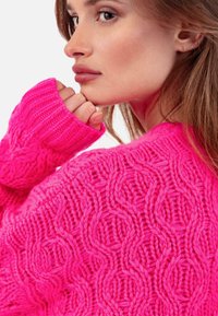 Helles pinkfarbenes Strickpullover mit strukturierten, miteinander verflochtenen Mustern. Lange Ärmel mit gerippten Bündchen, die ein grobes Garn-Design zeigen.