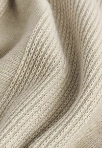 Beige pletená tkanina s jemnými a hrubými žebry, s měkkou texturou a jemnými barevnými variacemi po celém povrchu.