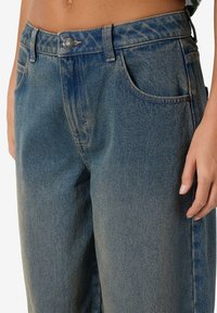 Høytlivs blå denimjeans med avslappet passform, fem lommer og subtil falming. Har metallknapp og glidelås-lukking, synlige sømdetaljer.