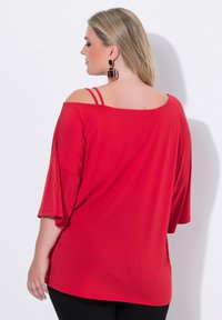 Rode off-the-shoulder top met korte mouwen, voorzien van dubbele spaghetti-bandjes. Soepele textuur, losse pasvorm en een gebogen zoomlijn.