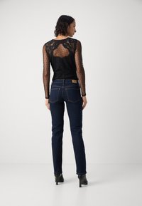 Camiseta negra de manga larga con encaje y malla de lunares, combinada con jeans oscuros de denim. Los jeans tienen un corte clásico y costuras sutiles.