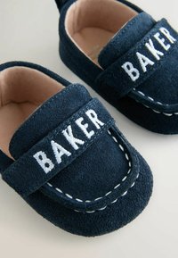 Meresinine seemisnahast mokassiinid, millel on valged tikitud aktsendid ja rihmal "BAKER" tikand. Pehme tan-värvi vooder mugavuse jaoks.