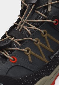 Κοντινή λήψη σκούρου αδιάβροχου παπουτσιού πεζοπορίας με κορδόνια σε μπεζ και πορτοκαλί αποχρώσεις που περνούν μέσα από ενισχυμένες οπές.