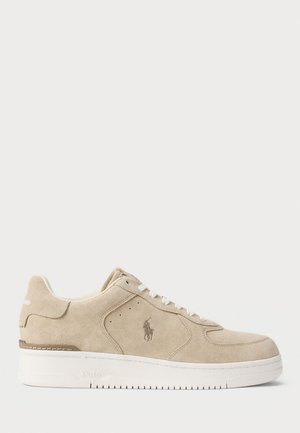 Beige semsket sko med hvit gummisåle, rund tå og snørelukking. Har logo-detalj og aksentsting på sidene.