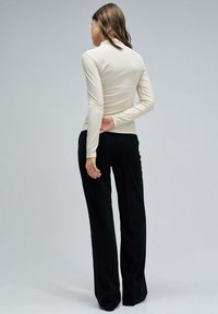 Top de manga larga color crema hecho de tela elástica, combinado con pantalones negros de cintura alta. Textura suave con silueta ajustada.