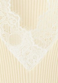 Tissu côtelé crème avec un délicat galon en dentelle florale blanche le long d'un décolleté en V.