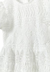 Robe blanche en dentelle présentant des motifs floraux élaborés, des couches texturées et des manches ballons. Doublure lisse et encolure ronde.