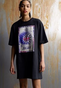 Black oversized t-shirt made of cotton, featuring a graphic print with a compass design and text. Short sleeves and a relaxed fit.