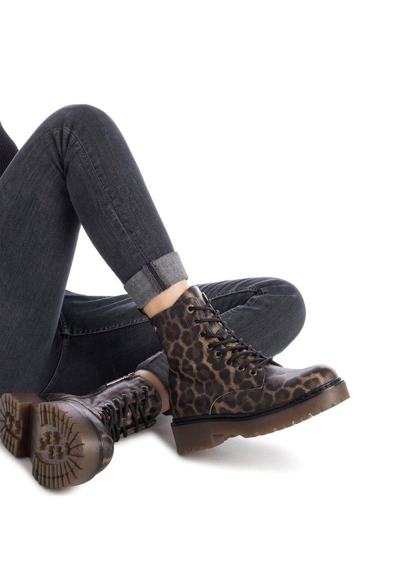 Botas de tobillo de estampado de leopardo con cordones negros y una suela gruesa y texturada. Llevadas con vaqueros oscuros que presentan los puños enrollados en un acabado gris más claro.