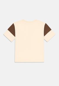 T-shirt à manches courtes de couleur beige avec des accents marron foncé sur les épaules, présentant un col rond classique et une coupe décontractée. Texture de tissu lisse.