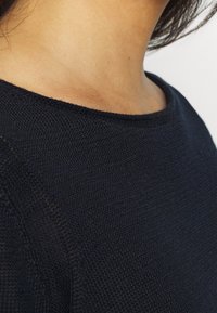 Granatowy sweter dzianinowy z okrągłym dekoltem, charakteryzujący się fakturowanym materiałem i gładkim wykończeniem, zbliżenie na detal kołnierza i ścieg.