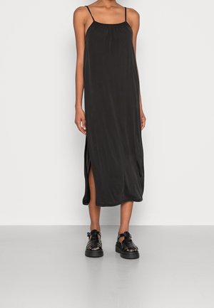 Black midi dress with adjustable spaghetti straps, a gathered neckline, and side slits. Worn with chunky black sandals. Smooth fabric texture.