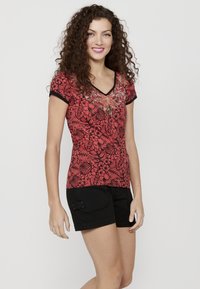 Chemise à manches courtes à motifs floraux rouges avec un col en V, rehaussée de finitions noires et d'ornements, assortie à un short noir.