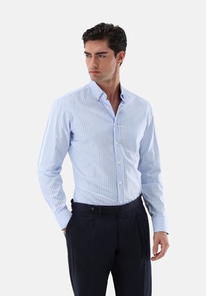 Camicia a righe blu chiaro e bianca con colletto button-down, taschino sul petto e maniche lunghe, abbinata a pantaloni scuri.