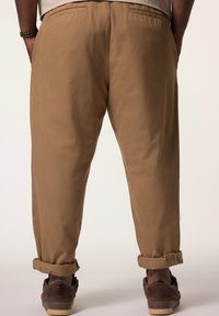 Hellbraune Chinohosen mit lässiger Passform, umgeschlagenen Säumen und Gesäßtaschen. Kombiniert mit dunkelbraunen Sneakers für den Kontrast.