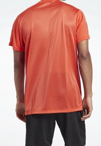 Camisa deportiva de manga corta en un brillante color naranja, con una textura de malla para mayor transpirabilidad. La vista trasera muestra un ajuste relajado. Se combina con pantalones cortos negros.